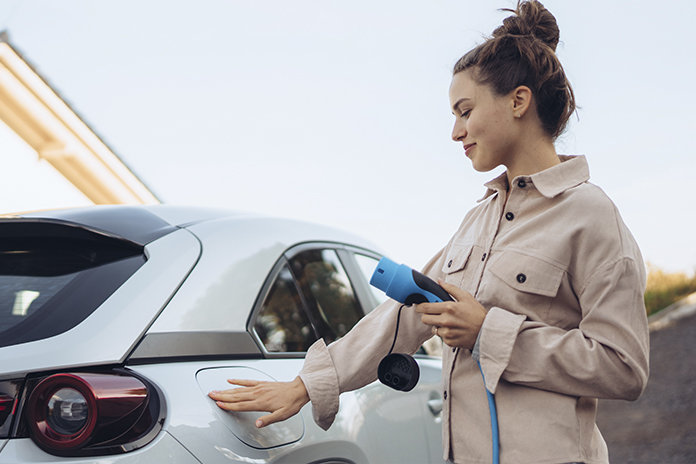 Chica abriendo la tapa del cargador de un coche eléctrico