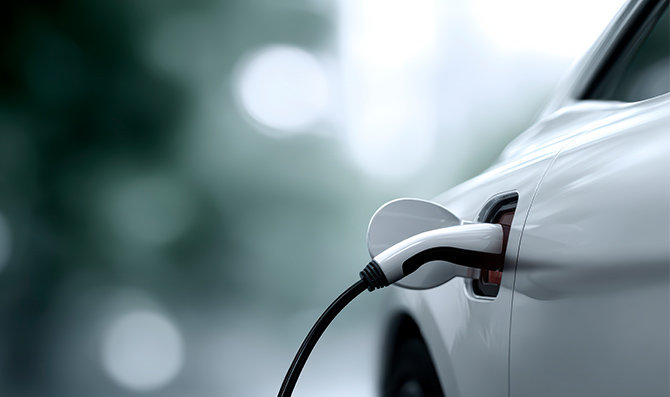 Detalle de un vehículo eléctrico conectado a un punto de carga, con el cable enchufado al lateral del coche en un entorno desenfocado
