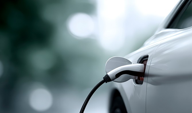 Detalle de un vehículo eléctrico conectado a un punto de carga, con el cable enchufado al lateral del coche en un entorno desenfocado