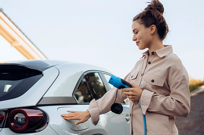 Mujer joven cargando un coche eléctrico, conectando el cable de carga en el lateral del vehículo