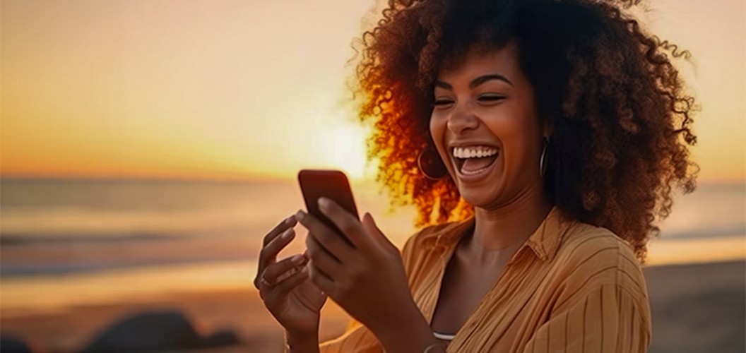 Persona utilizando un teléfono móvil frente al mar durante el atardecer, con tonos cálidos reflejados en el horizonte